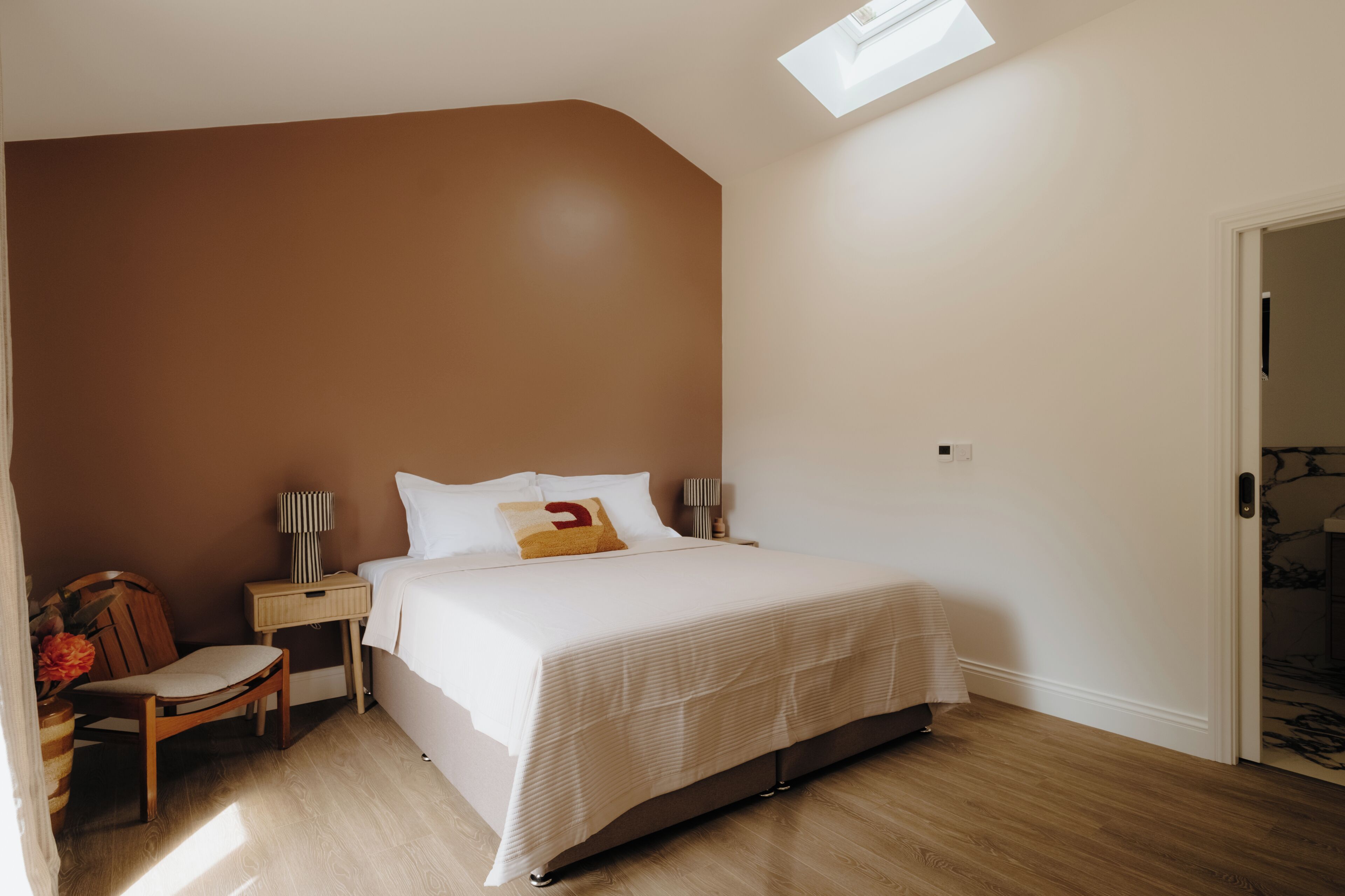 Une chambre à coucher avec un lit, une chaise, une table de chevet, une lampe et une lucarne.