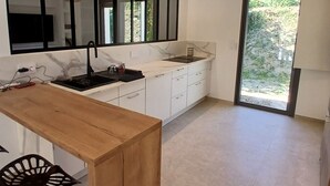 Moderni keittiö, jossa on puinen pöytä, mustat riippuvalaisimet, valkoiset kaapit ja suuri ikkuna.
