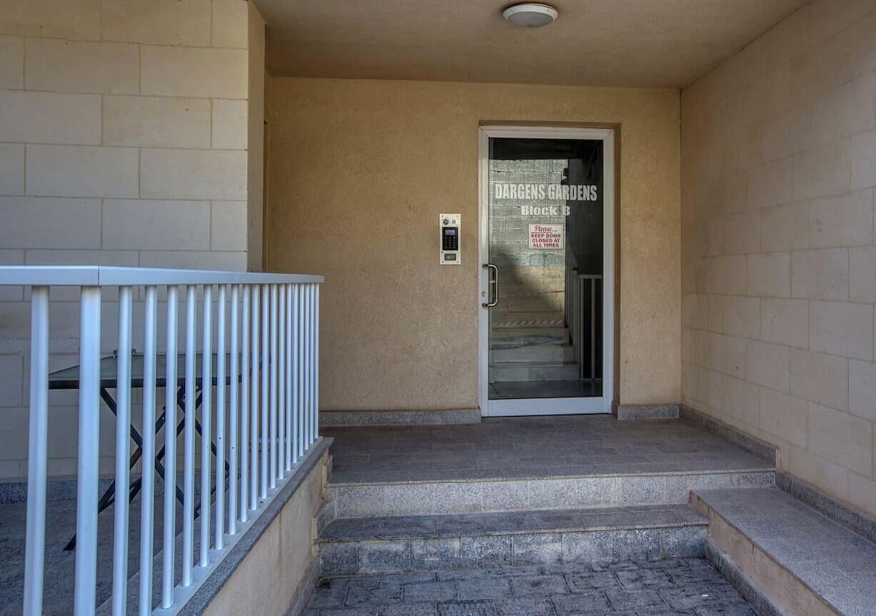 A building entrance with a metal railing, a door labeled 'DARGENS GARDENS Block B,' and a security keypad.