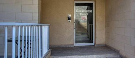 A building entrance with a metal railing, a door labeled 'DARGENS GARDENS Block B,' and a security keypad.