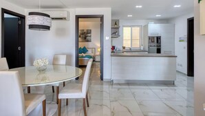 Una cucina moderna con isola centrale, zona pranzo con tavolo in vetro e soggiorno con divano e opere d'arte.