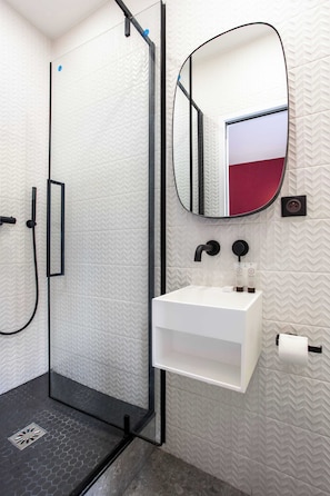 Une salle de bain moderne avec une douche à parois de verre, un lavabo blanc, un miroir et un porte-serviettes.