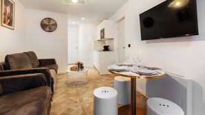 A modern living room with a sofa, a dining table set with plates and glasses, a mounted TV, a clock, and a pendant light. - Palette Paris Tour Eiffel (Paris)