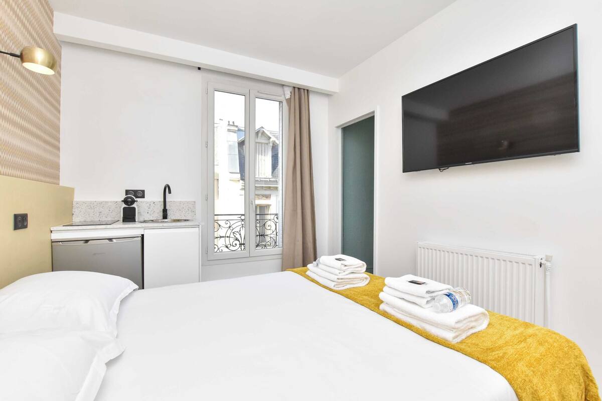 A hotel room with a bed, a TV, a small kitchenette, and a balcony with a view.