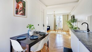 A modern kitchen with a dark countertop, white chairs, and a dining table set for four. - Palette Paris Tour Eiffel (Paris)