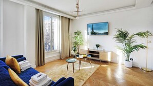 A modern living room with a blue sofa, a wooden floor, a white wall, a painting, and a potted plant. - Palette Paris Tour Eiffel (Paris)