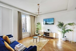 Un salon moderne avec un canapé bleu, un plancher en bois, un mur blanc, un tableau et une plante en pot.