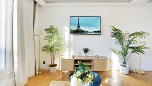 A living room with a large window, a wooden floor, a white sofa, a coffee table with flowers, and a painting of the Eiffel Tower. - Palette Paris Tour Eiffel (Paris)
