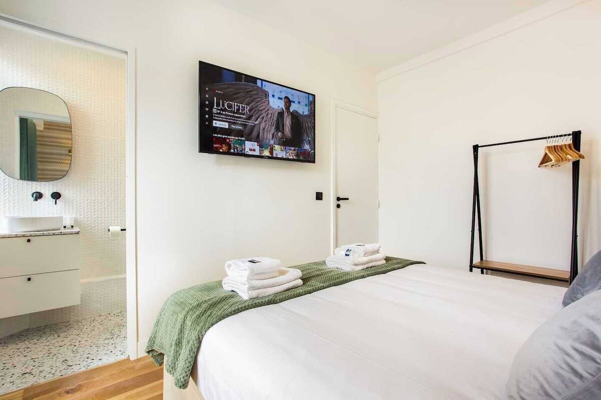 A hotel room with a bed, a television mounted on the wall, a mirror, a wardrobe, and a wooden floor.