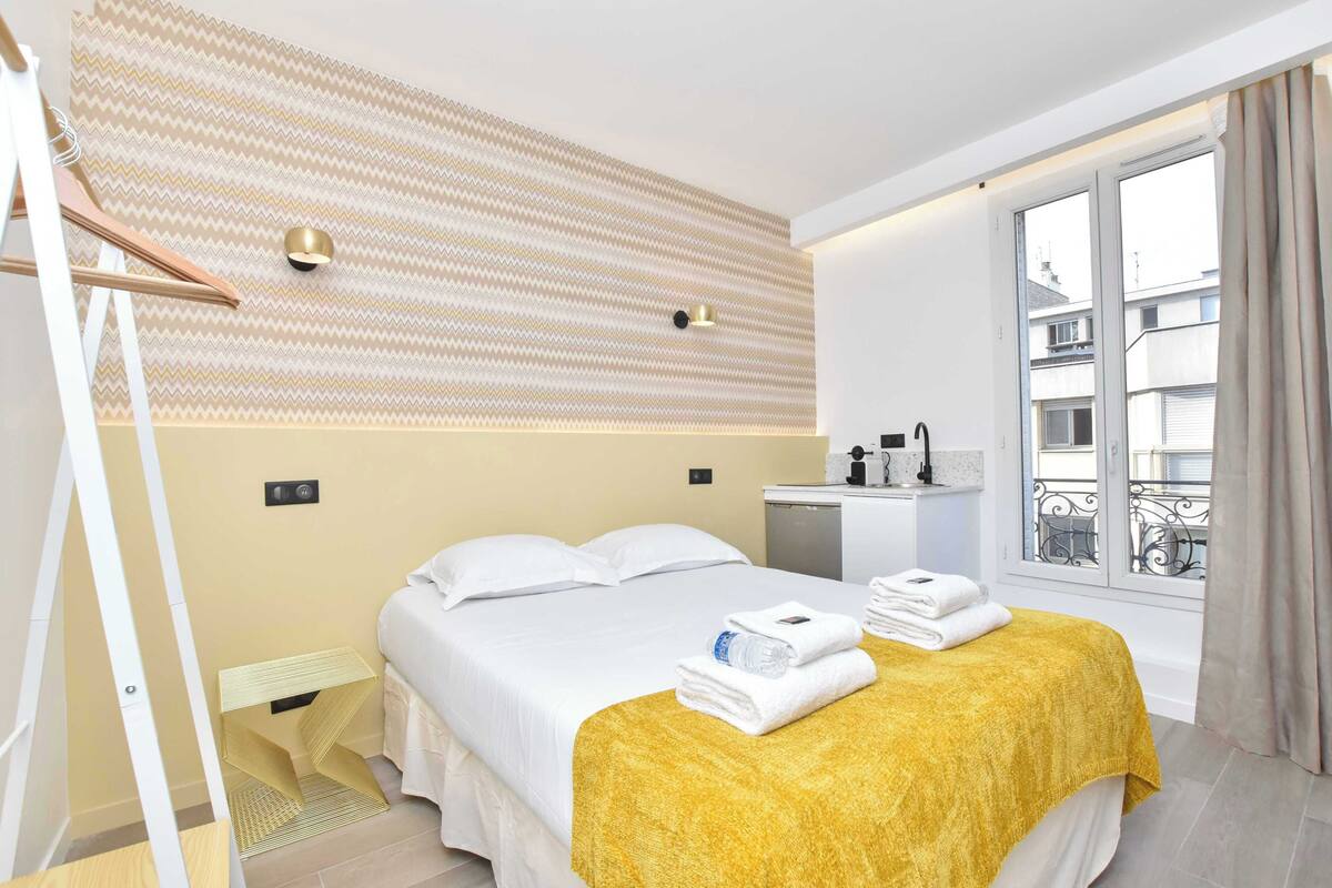 A hotel room with a bed, a small desk, a window with a view, and a patterned wall.