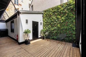 Eine Holzterrasse mit einem weißen Gebäude, einer schwarzen Tür und einer grünen Wand mit roten Blumen.