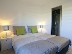 Ein Doppelbett mit zwei Kissen, ein Nachttisch mit Lampe sowie ein Duschbereich.