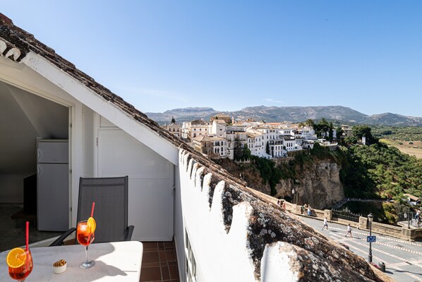 A balcony with a view of a town, a table with drinks, and a refrigerator.