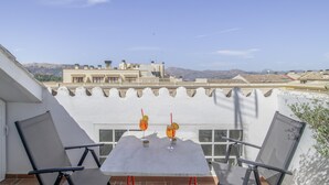 Una terraza con una mesa y dos sillas, con vistas a un paisaje urbano y montañas a lo lejos.