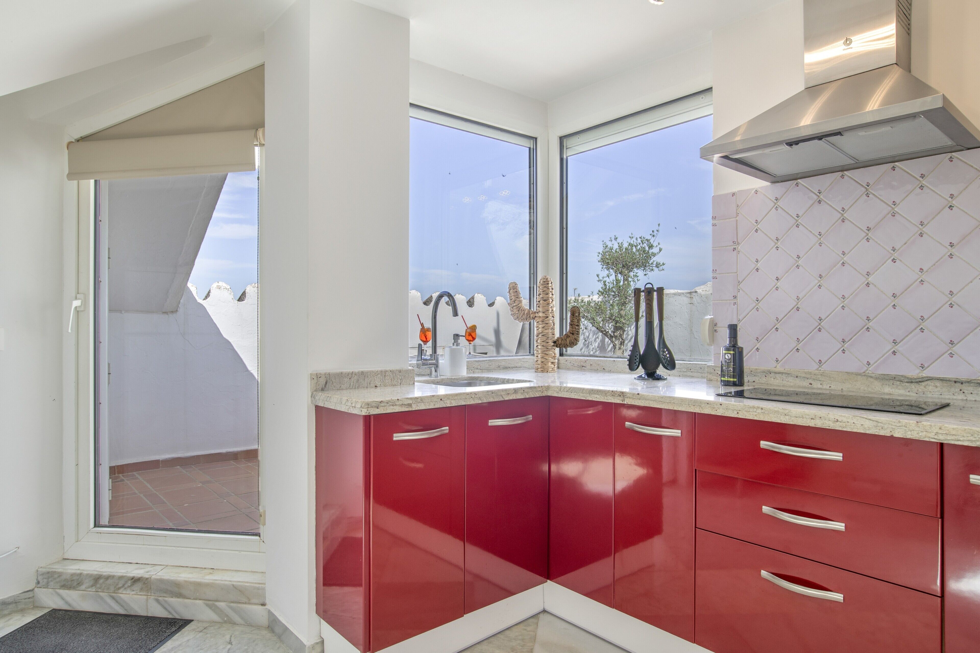 Una cocina moderna con armarios rojos, una campana extractora de acero inoxidable y un amplio ventanal con vistas al exterior.