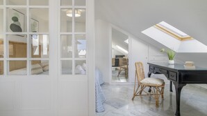 Una habitación con tragaluz, una zona de comedor con mobiliario de mimbre y un escritorio negro.
