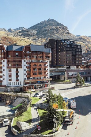 A multi-story hotel with balconies, a ski resort in the background, and a parking area with a road leading to the hotel. - Cimes de Caron Val Thorens (Val Thorens)
