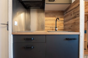 Una cocina con protector de pared de madera, un grifo negro y dos gabinetes negros con pomos.