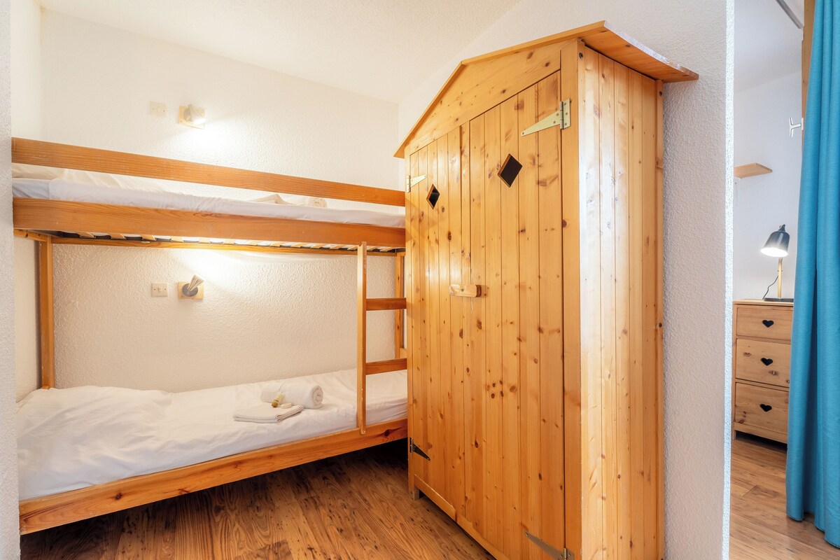 A bunk bed room with a wooden wardrobe and a desk with drawers.