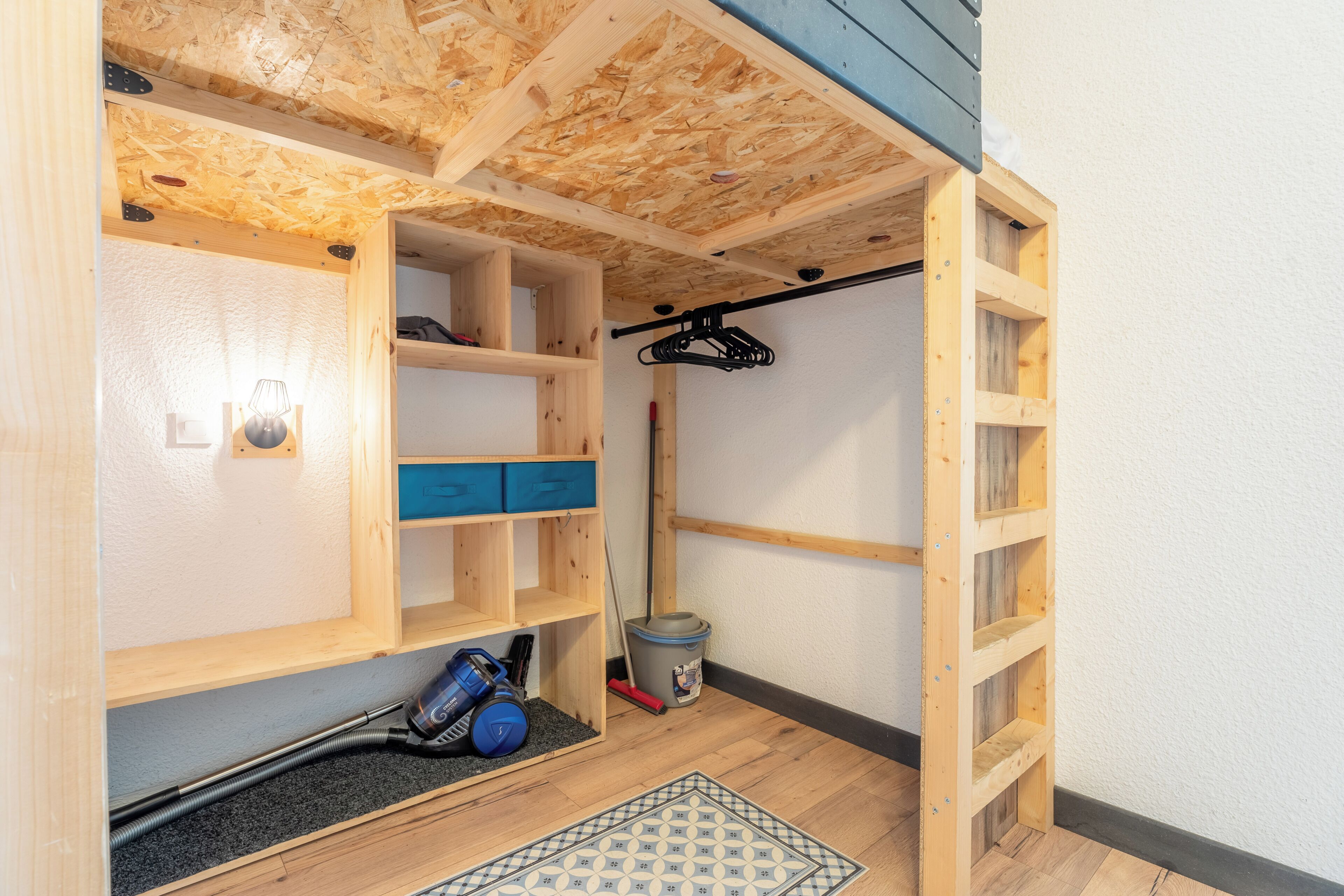 A compact storage room with wooden shelving, a vacuum cleaner, and a broom.