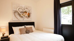 A hotel room with a bed, a nightstand, a lamp, a window with curtains, and a wall art piece. - Holiday Home in Belfeld With Terrace (Belfeld)