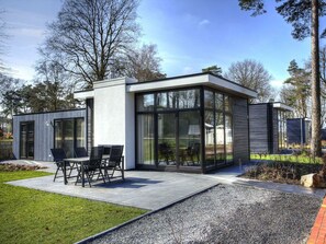 Ein modernes Haus mit Terrasse, einem Essbereich mit Stühlen und einem großen Fenster.
