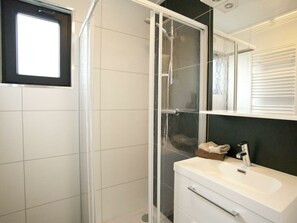 Ein modernes Badezimmer mit Duschkabine aus Glas, einem weißen Waschbecken und einem Spiegel darüber.