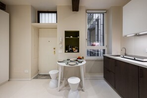 Eine kleine Küche mit Esstisch, Hocker, einem Fenster und einer integrierten Ablage.