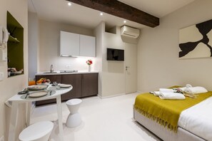 Ein modernes Hotelzimmer mit Bett, Esstisch, Küchenzeile und Bad.