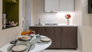 Une cuisine moderne avec un plan de travail blanc, des meubles de rangement en bois foncé, un four encastré et un petit coin repas avec une table dressée pour deux personnes.