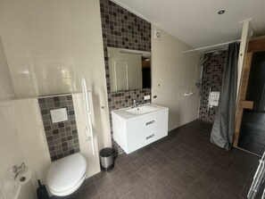 Ein Badezimmer mit Toilette, Waschbecken, Spiegel und Duschbereich.