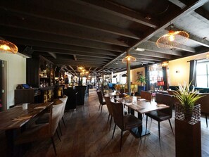 Ein Restaurantinneres mit Holztischen und -stühlen, hängenden Pendelleuchten und einer Bar.