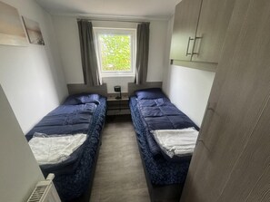 Ein kleines Zimmer mit zwei Betten, einem Fenster und einer Heizung.