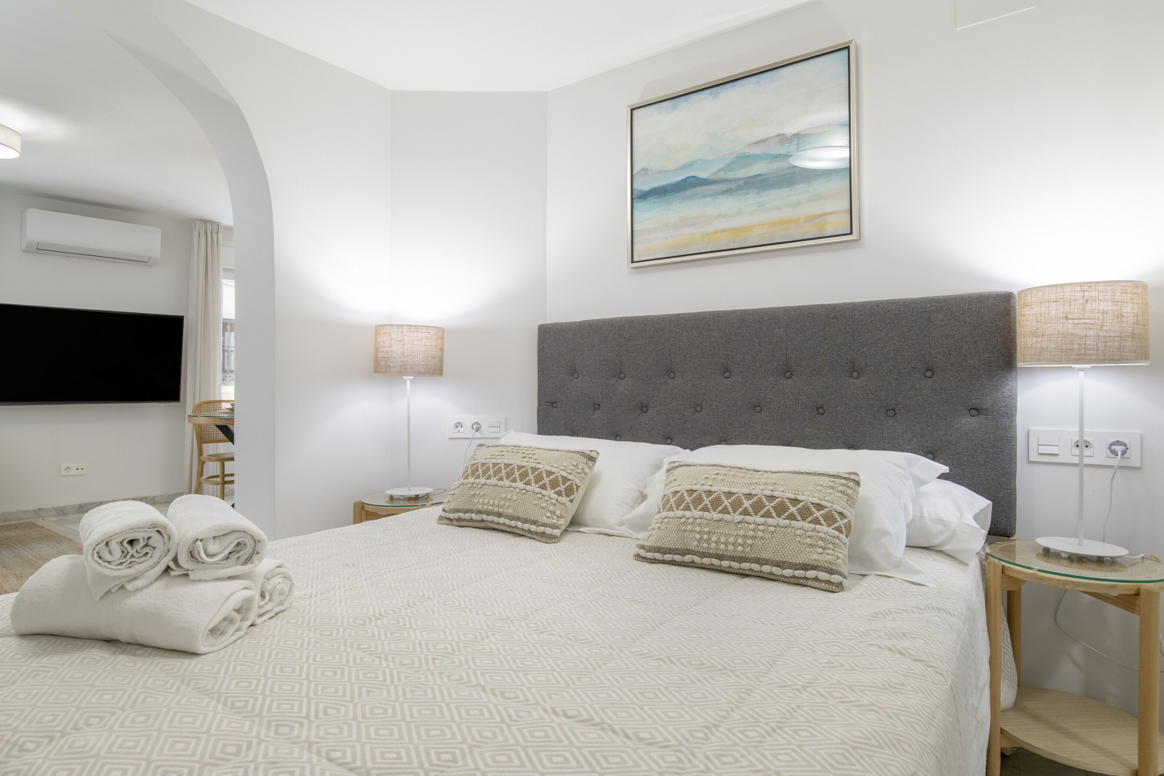 Une chambre d’hôtel avec un lit, deux lampes de chevet, un téléviseur à écran plat et un tableau au mur.