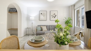 Ein modernes Wohnzimmer mit Essbereich, grauem Sofa, Kunstwerk an der Wand und einem Wand-Fernseher.