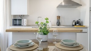 Eine moderne Küche mit weißen Schränken, einer Edelstahl-Dunstabzugshaube, einer Mikrowelle und einer Kaffeemaschine. Es gibt eine Holz Arbeitsplatte mit einer Pflanze und einem Weinglas.