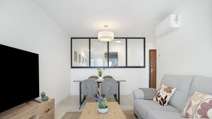 Una sala de estar moderna con un televisor de pantalla plana, un sofá, una mesa de centro con una planta y una zona de comedor con sillas y una mesa.