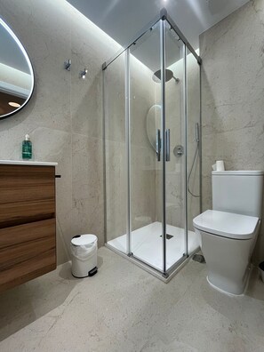 Ein modernes Badezimmer mit einer gläsernen Duschkabine, einem Holzwaschtisch, einer Toilette und einer Wand mit Marmorfliesen.
