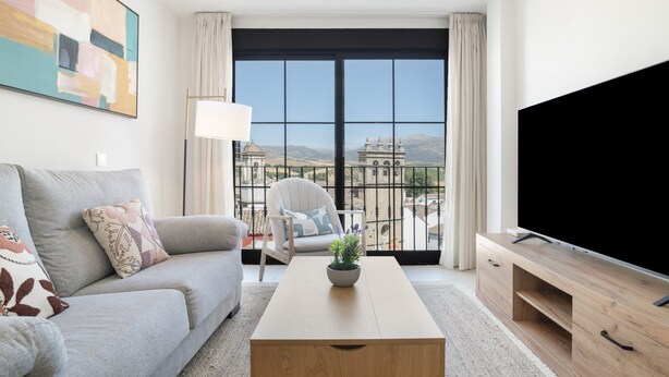 Una sala de estar moderna con un sofá, una mesa de centro, un televisor y un balcón con vistas a edificios.