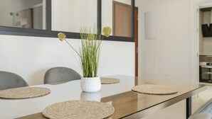 Una mesa de comedor con un florero blanco que contiene plantas verdes, rodeada de cuatro individuales tejidos.