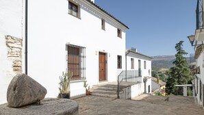 Un edificio blanco con puerta de madera, un banco de piedra y macetas.