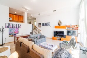 Ein modernes Wohnzimmer mit Sofa, Couchtisch und Fernseher. Eine Treppe führt auf eine höhere Ebene.