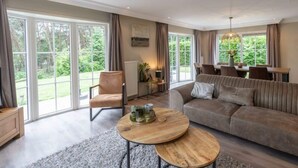 Een ruime woonkamer met een bank, een rond bijzettafeltje en een fauteuil.