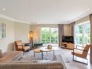 A modern living room with a sofa, coffee table, and TV, large windows, and a view of greenery. - Hackfort L"etage 8 (Brunssum)