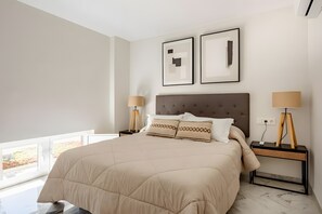 Une chambre à coucher avec un grand lit, deux tables de chevet avec des lampes et des œuvres d’art encadrées accrochées au mur.
