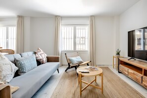 Ein modernes Wohnzimmer mit einer Couch, Sesseln, einem Couchtisch, einem Fernseher und einem Holzschrank.