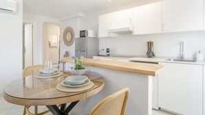 A modern kitchen with white cabinetry, a wooden countertop, and a dining area with a glass table and wicker chairs.