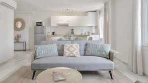 A modern living room with a grey sofa, patterned cushions, a coffee table, and a kitchen in the background.