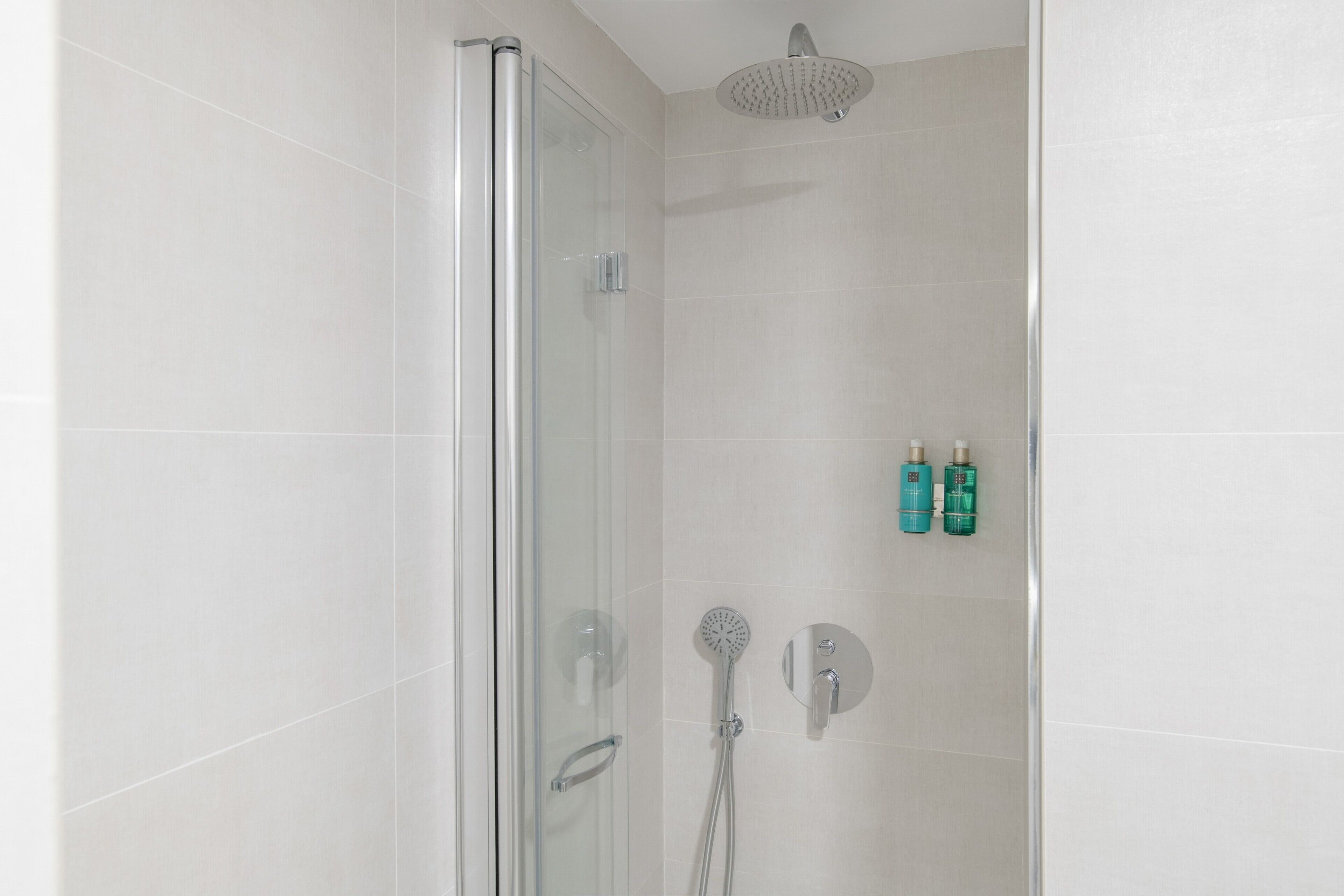 A glass-enclosed shower with a handheld showerhead and a wall-mounted control panel.
