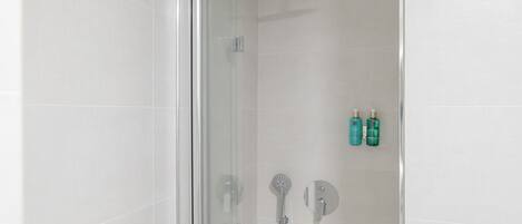 A glass-enclosed shower with a handheld showerhead and a wall-mounted control panel.